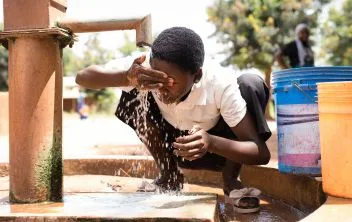 Niña lavándose la cara en fuente de agua